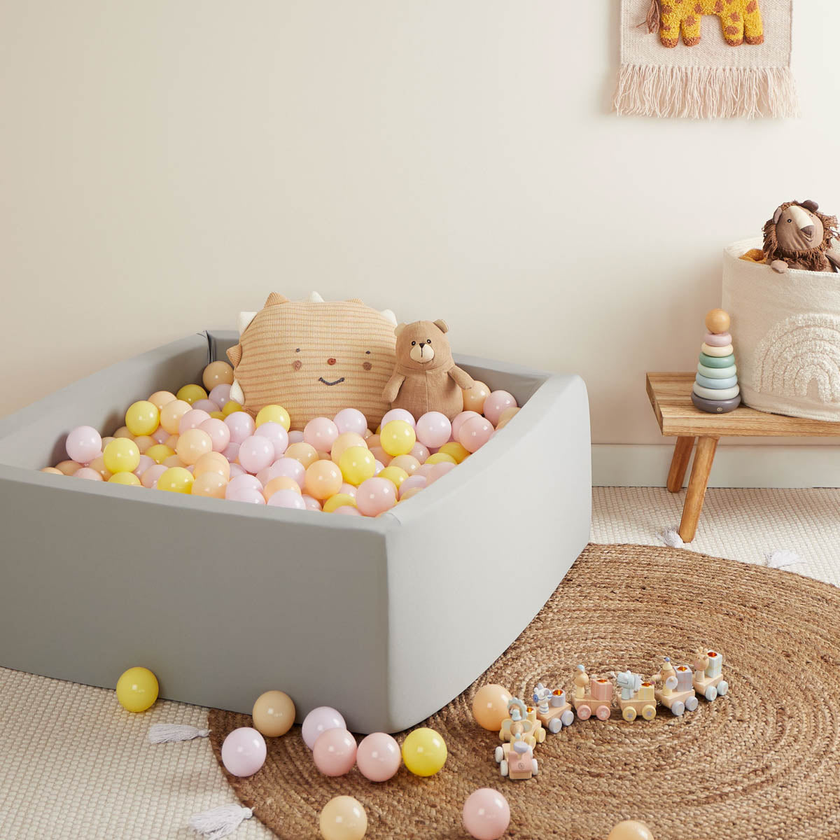 Kinderzimmer mit grauem Bällebad und pastellfarbenen Bällen in hellrosa, gelb und peach.