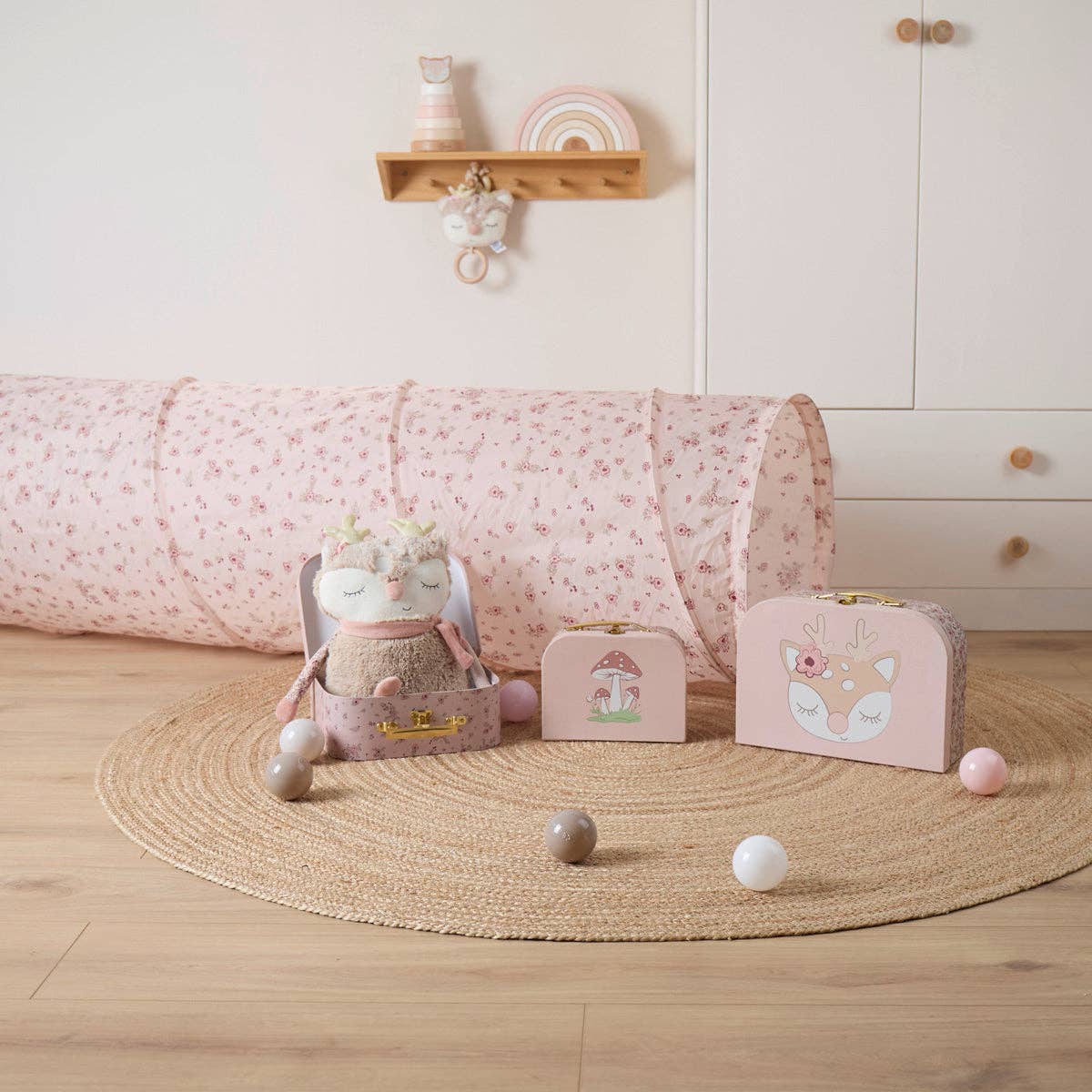 Kinderzimmer mit rosafarbenem Spieltunnel mit Blümchenmuster und passenden Spielkoffern.