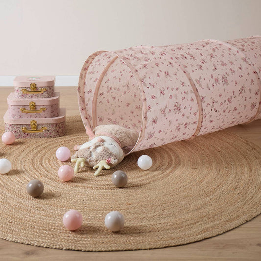 Kinderzimmer mit altrosa Spieltunnel mit Blümchendesign, farblich passenden Bällen aus einem Bällebad sowie Spielkoffern. 